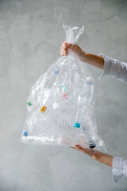 A person wearing a long-sleeved, light-colored striped shirt is holding a large, transparent plastic bag filled with various clear and coloured plastic bottles and containers. The bag is gripping the 